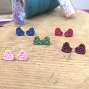 Χειροποίητα σκουλαρίκια μακραμέ σε σχήμα καρδιάς σε διάφορα χρώματα πάνω σε ξύλινη επιφάνεια