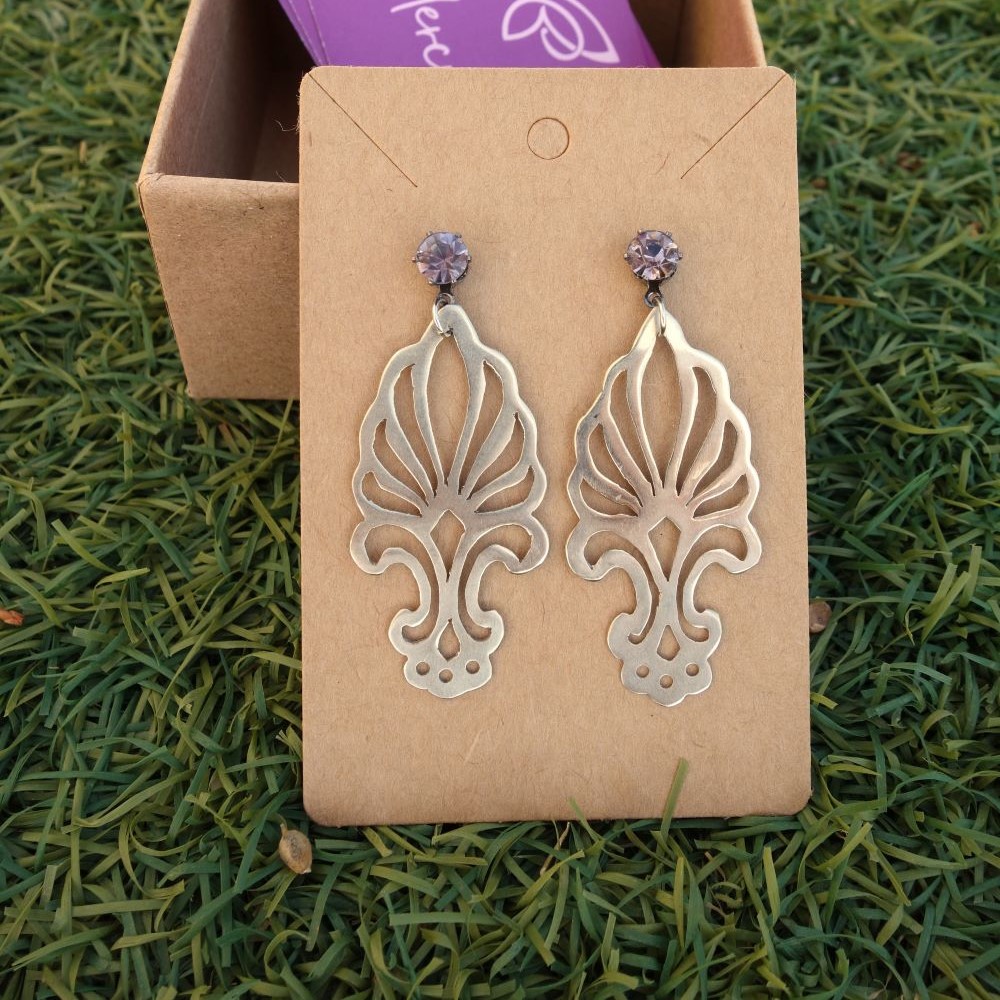 Χειροποίητα διάτρητα σκουλαρίκια από απλακά με κρυστάλλινη λεπτομέρεια, τοποθετημένα σε χάρτινη βάση μπροστά σε φυσικό φόντο.