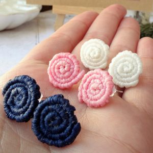 Χειροποίητα σκουλαρίκια μακραμέ σε σχέδιο σπείρας σε λευκό, ροζ και μπλε, πάνω σε χέρι.