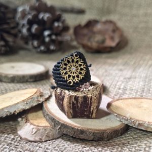 Μαύρο μακραμέ δαχτυλίδι με ατσάλινη χιονονιφάδα επάνω σε ξύλινη βάση.