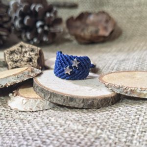 Μπλε μακραμέ δαχτυλίδι με ατσάλινα αστεράκια επάνω σε ξύλινη βάση.