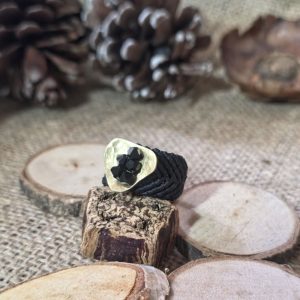 Μαύρο μακραμέ δαχτυλίδι με χειροποίητο ορειχάλκινο στοιχείο και μαύρα κρυσταλλάκια επάνω σε ξύλινη βάση.