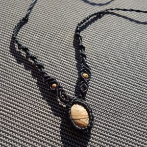 Μαύρο μακραμέ κολιέ με πέτρα Ιάσπη Picture και μικρές χρυσές χάντρες σε γκρι φόντο.