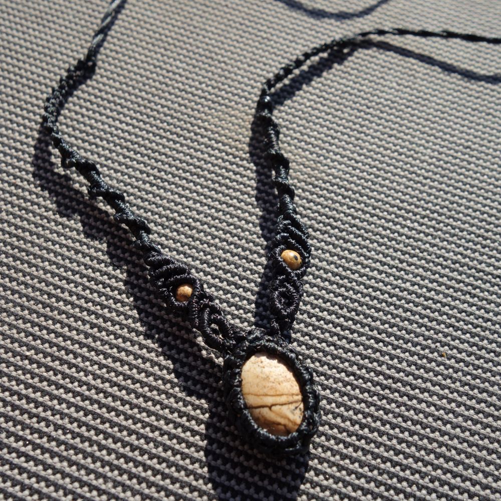 Μαύρο μακραμέ κολιέ με πέτρα Ιάσπη Picture και μικρές χρυσές χάντρες σε γκρι φόντο.