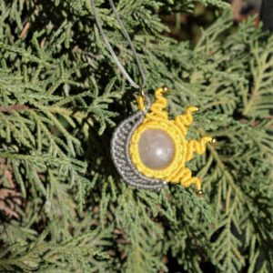 Μακραμέ κολιέ ήλιου–φεγγαριού με λευκό χαλαζία σε γκρι–κίτρινη πλέξη, φωτογραφημένο επάνω σε φύλλα.