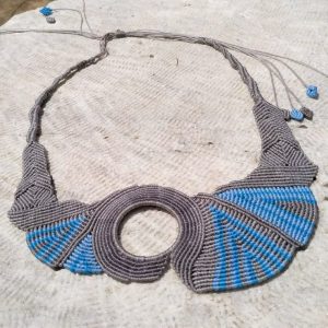 Statement γκρι και γαλάζιο μακραμέ κολιέ με κεντρικό κυκλικό άνοιγμα, τοποθετημένο σε ανοιχτό φόντο.