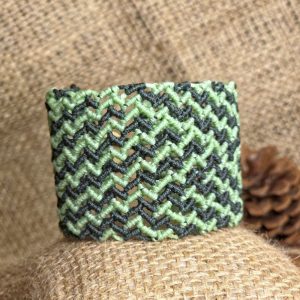 Χειροποίητο μακραμέ βραχιόλι σε κυπαρισσί και ανοιχτό πράσινο με γεωμετρικό σχέδιο και κούμπωμα πάνω σε φυσικό φόντο