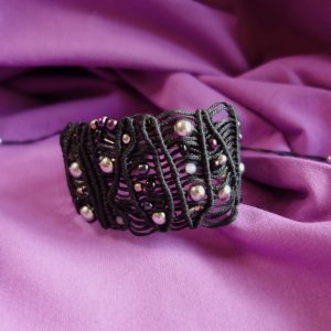 Χειροποίητο μαύρο μακραμέ βραχιόλι με μεταλλικές χάντρες και αυξομείωση πάνω σε μωβ ύφασμα