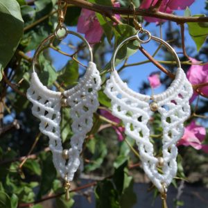 Χειροποίητα μακραμέ σκουλαρίκια σε λευκό γκρι και κόκκινο κρεμασμένα σε κλαδί με λουλούδια
