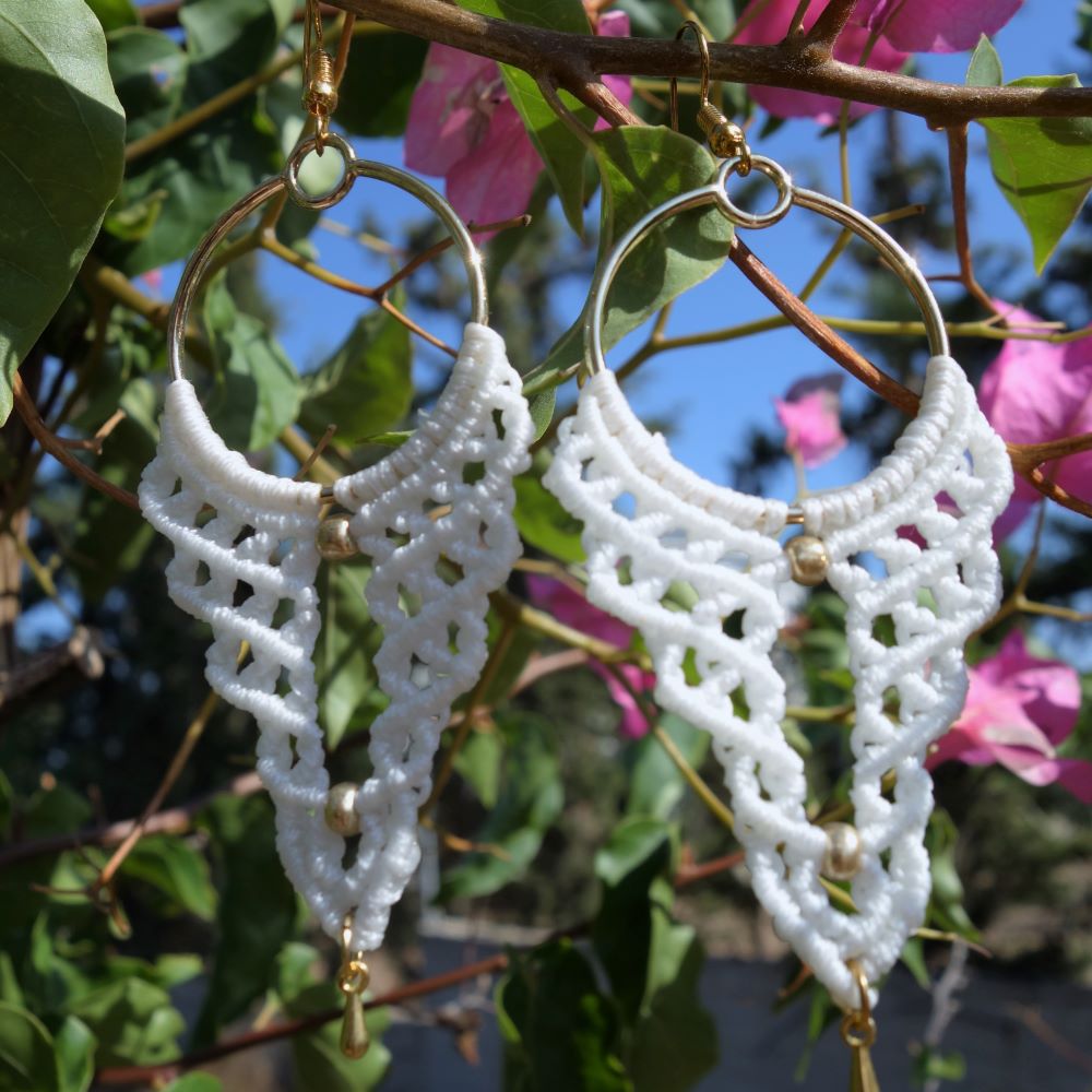 Χειροποίητα μακραμέ σκουλαρίκια σε λευκό γκρι και κόκκινο κρεμασμένα σε κλαδί με λουλούδια