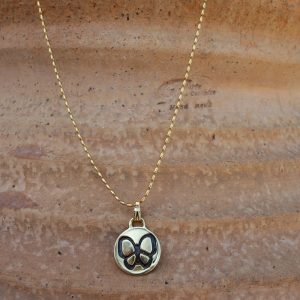 Χειροποίητο ορειχάλκινο κολιέ με πατίνα και πεταλούδα σε κυκλικό σχήμα πάνω σε φυσικό φόντο