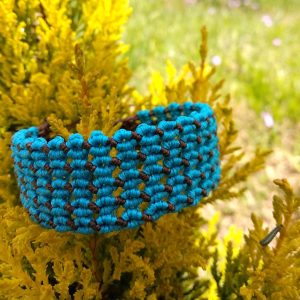 Χειροποίητο μακραμέ βραχιόλι σε τιρκουάζ και καφέ με γεωμετρικό σχέδιο πάνω σε φυσικό φόντο