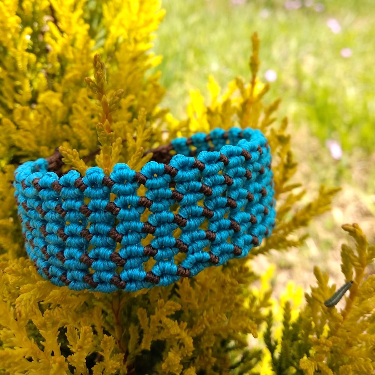 Χειροποίητο μακραμέ βραχιόλι σε τιρκουάζ και καφέ με γεωμετρικό σχέδιο πάνω σε φυσικό φόντο